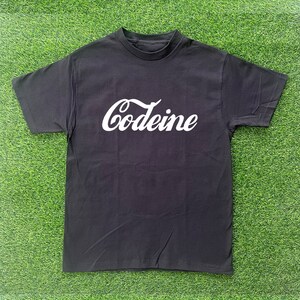 Puede incluir: Camiseta negra con un gráfico blanco de "Codeine" en una fuente inspirada en Coca-Cola.