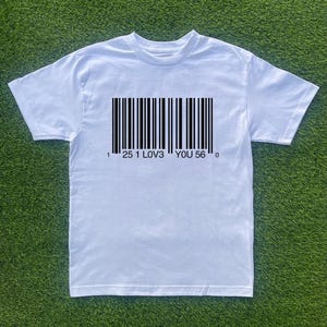 Op de afbeelding: Wit T-shirt met een zwarte barcode-afbeelding en de tekst "1 25 1 LOV3 YOU 56 0".