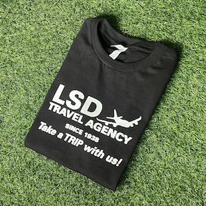 May include: Black t-shirt with white text that reads "LSD Travel Agency Since 1938 Take a TRIP with us!" and a white airplane graphic.