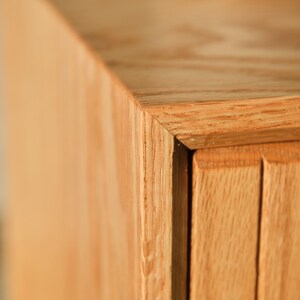 Puede incluir: Primer plano de una esquina de un mueble de madera. El mueble es de madera clara con veta natural. La esquina est&aacute; unida con precisi&oacute;n, mostrando la artesan&iacute;a. El dise&ntilde;o presenta ranuras verticales en el lateral.