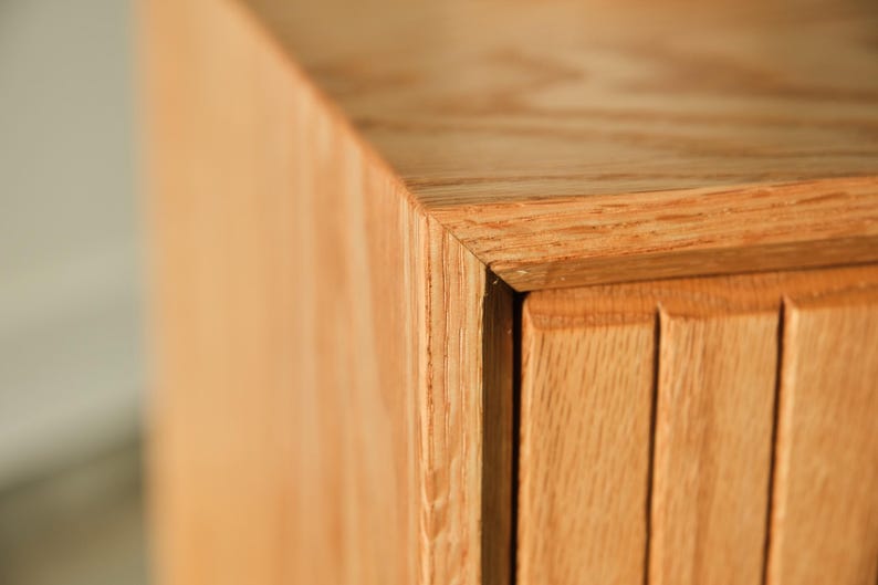 Puede incluir: Primer plano de una esquina de un mueble de madera. El mueble es de madera clara con veta natural. La esquina est&aacute; unida con precisi&oacute;n, mostrando la artesan&iacute;a. El dise&ntilde;o presenta ranuras verticales en el lateral.