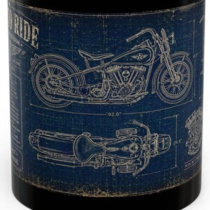 May include: A black ceramic mug featuring a blue and beige technical blueprint design of a motorcycle. The graphic includes side and top views of the bike with technical lines, measurements, and the text "BORN TO RIDE" printed on the side.