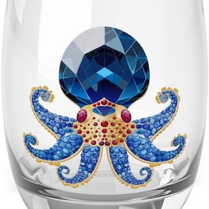 May include: A clear stemless wine glass featuring a detailed blue octopus design. The octopus has a large, faceted blue head, blue tentacles, and gold and red accents. The glass is ideal for serving wine or other beverages.