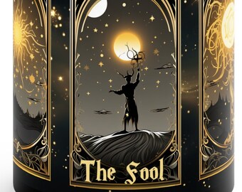 May include: Black coffee mug with a gold design featuring a tarot card illustration of The Fool. The card depicts a figure standing on a hilltop with a starry night sky and a crescent moon in the background.