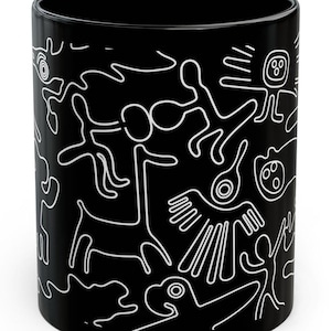 May include: Black ceramic mug featuring a white line art design of abstract figures and shapes. The design wraps around the mug, creating a continuous pattern. The mug is cylindrical and has a glossy finish.