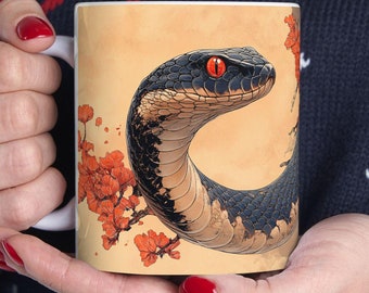 May include: White ceramic mug with a black and white snake with a red eye on a yellow background with red flowers.