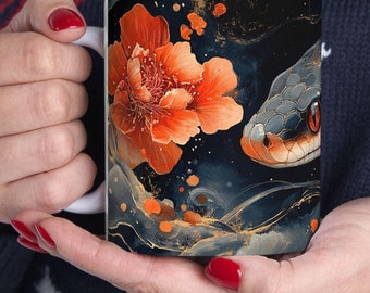 May include: White ceramic mug with a black, gold, and orange design. The design features a snake with a red eye and a large orange flower.
