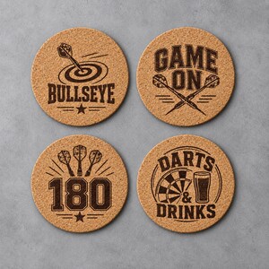 Op de afbeelding: Vier ronde onderzetters van kurk met donkerbruine, lasergegraveerde dart-ontwerpen. De ontwerpen bevatten een dartpijl in de roos, de tekst GAME ON met gekruiste darts, het getal 180 met drie darts en een dartbord met een glas bier.