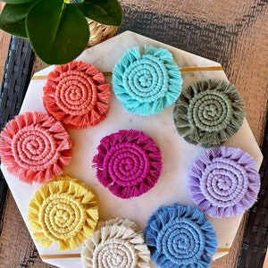 May include: A set of ten colorful round crocheted coasters with fringe. The coasters are in various colors, including pink, blue, green, yellow, and white.