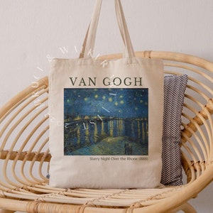 May include: A white canvas tote bag with a print of Vincent van Gogh's "Starry Night Over the Rhone" painting. The bag has black handles and the text "VAN GOGH" and "Starry Night Over the Rhone (1888)" printed on the front.