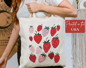 May include: A white tote bag featuring a red, pink and green strawberry pattern. The bag has a black handle and the text "Printed in the USA" is printed on a red tag.