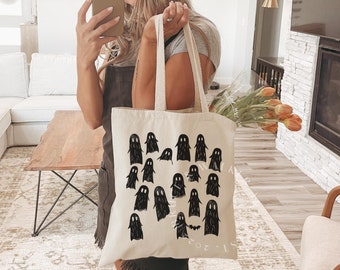 May include: A white canvas tote bag featuring black ghost illustrations and a bat graphic. The text "It's the most wonderful time of the year" is printed on the bag.