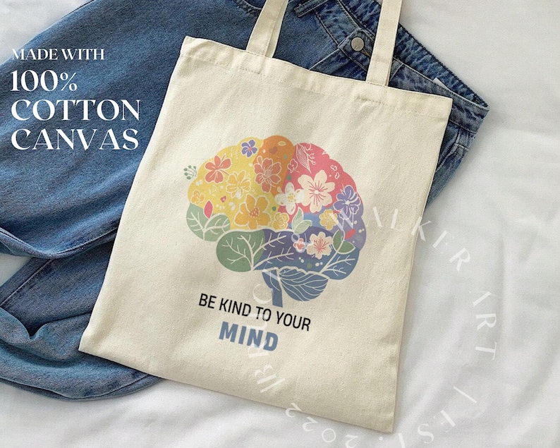 May include: A beige tote bag made with 100% cotton canvas. The bag features a colorful brain design with flowers and the text "Be Kind to Your Mind".