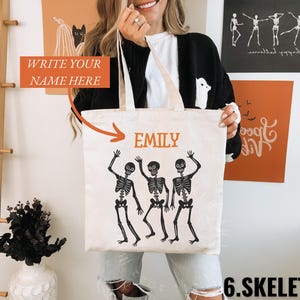 May include: A white canvas tote bag with a black design of three skeletons dancing. The bag has a black handle and the text "EMILY" is printed on the front.