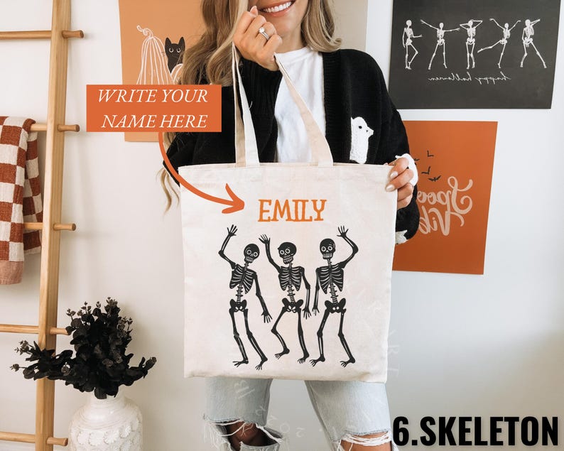 May include: A white canvas tote bag with a black design of three skeletons dancing. The bag has a black handle and the text "EMILY" is printed on the front.