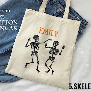 May include: A white canvas tote bag with black skeleton figures and the text "Emily" printed in orange. The bag is made with 100% cotton canvas.