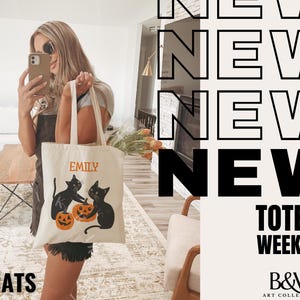 May include: A white tote bag with black cats and pumpkins. The bag has the name "Emily" printed on it. The text "NEW TOTES WEEKLY" and "B&W ART COLLECTIVE" are also visible. The bag is being held by a person.