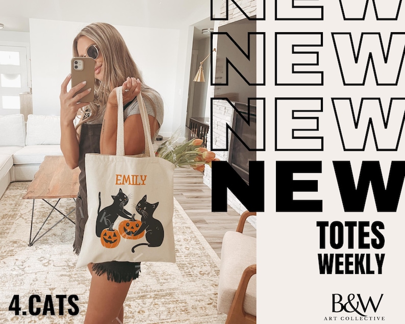 May include: A white tote bag with black cats and pumpkins. The bag has the name "Emily" printed on it. The text "NEW TOTES WEEKLY" and "B&W ART COLLECTIVE" are also visible. The bag is being held by a person.