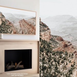 May include: A framed print depicting a canyon landscape with reddish-brown rock formations and green vegetation. The print is displayed above a fireplace. The text "THE DESERT COLLECTION" and "+100 ARTWORKS" is visible at the bottom.