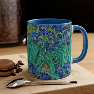 May include: A blue ceramic mug with a white interior and a handle. The mug features a colourful painting of irises, a famous artwork by Vincent van Gogh.