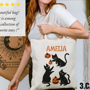 May include: A white canvas tote bag with black cats and pumpkins. The bag has the name "Amelia" printed on it and the text "3.CATS" at the bottom.