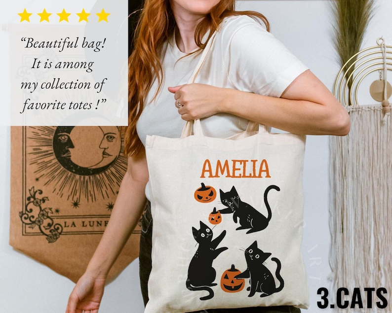 May include: A white canvas tote bag with black cats and pumpkins. The bag has the name "Amelia" printed on it and the text "3.CATS" at the bottom.