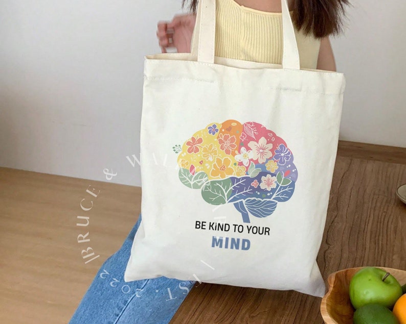 May include: A white tote bag with a colorful floral brain design and the text "Be kind to your mind".