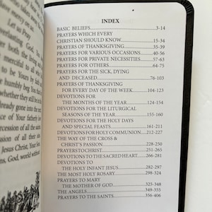May include: Open book with a black cover, displaying an index of prayers and devotions. The index includes topics such as basic beliefs, prayers for various occasions, and prayers to the saints. The pages are white with black text.