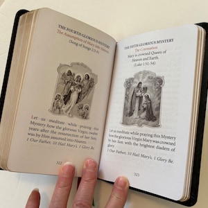 May include: Open book with black cover, displaying two pages with religious text and illustrations. The left page details "The Fourth Glorious Mystery" with an image of angels. The right page shows "The Fifth Glorious Mystery" with a coronation scene. Page numbers 322 and 323 are visible.