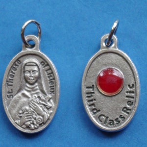 May include: Silver oval pendant with a picture of Saint Therese of Lisieux on one side and the words "Third Class Relic" and a red glass stone on the other side.