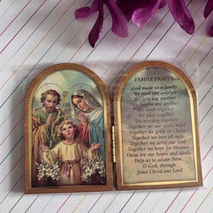 Puede incluir: Una caja de oraci&oacute;n de madera con un frente con bisagras. El frente presenta una pintura de la Sagrada Familia, con Jes&uacute;s, Mar&iacute;a y Jos&eacute;. La parte posterior de la caja tiene una oraci&oacute;n para las familias, que dice: "Dios nos hizo una familia, Nos necesitamos unos a otros, Nos amamos unos a otros, Nos perdonamos unos a otros, Trabajamos juntos, Jugamos juntos, Adoramos juntos, Juntos usamos la palabra de Dios, Juntos crecemos en Cristo, Juntos amamos a todos los hombres, Juntos servimos a nuestro Dios, Juntos esperamos el Cielo, Estas son nuestras esperanzas e ideales, Ay&uacute;danos a alcanzarlas, Oh Dios, a trav&eacute;s de Jesucristo nuestro Se&ntilde;or."