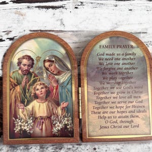 Puede incluir: Una caja de oraci&oacute;n de madera con un panel frontal con bisagras. El panel frontal presenta una pintura de la Sagrada Familia, con Jos&eacute;, Mar&iacute;a y Jes&uacute;s. El panel posterior tiene una oraci&oacute;n para las familias, que dice: "Dios nos hizo una familia. Nos necesitamos unos a otros. Nos amamos unos a otros. Nos perdonamos unos a otros. Trabajamos juntos. Jugamos juntos. Adoramos juntos. Juntos usamos la palabra de Dios. Juntos crecemos en Cristo. Juntos amamos a todos los hombres. Juntos servimos a nuestro Dios. Juntos esperamos el Cielo. Estas son nuestras esperanzas e ideales. Ay&uacute;danos a alcanzarlas, oh Dios, a trav&eacute;s de Jesucristo nuestro Se&ntilde;or."