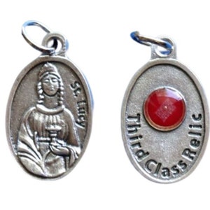 May include: Two silver-toned oval pendants. One pendant features an engraved image of St. Lucy with the text "St. Lucy". The other pendant has a red gemstone and the text "Third Class Relic".