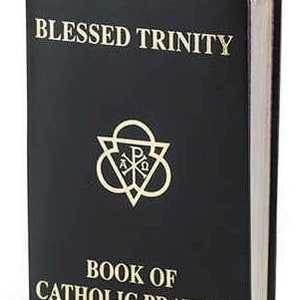 May include: A black book with gold lettering that reads "BLESSED TRINITY" and "BOOK OF CATHOLIC PRAYERS." A gold emblem is centered below the title. A colorful ribbon bookmark is visible at the top. The book's pages have a gold edge.