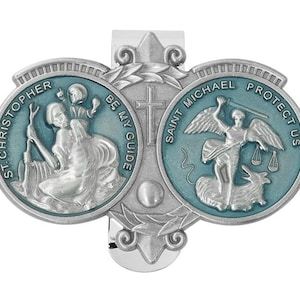 May include: A silver-toned religious clip featuring two teal-colored medallions. One depicts St. Christopher with a child, the other St. Michael. Text includes "St. Christopher Be My Guide" and "Saint Michael Protect Us".