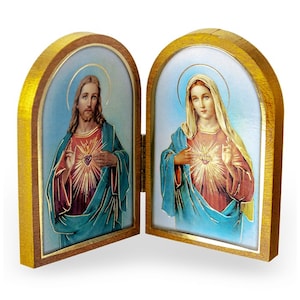 May include: A hinged, wooden religious icon featuring two panels. Each panel displays a portrait with a gold halo and a heart with radiating light. The portraits are set against a blue background, framed by gold trim and a wooden border.