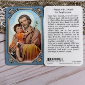 May include: A prayer card featuring an illustration of Saint Joseph holding a child, with a blue border and gold accents. The reverse side has a prayer for employment. The card is made in Italy.
