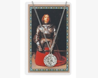 May include: A silver-toned necklace with a pendant featuring an image of Saint Joan of Arc. The pendant hangs in front of a card with a portrait of Joan of Arc in armor. The card has a decorative border and the words "Saint Joan of Arc" and "Pray for Us".