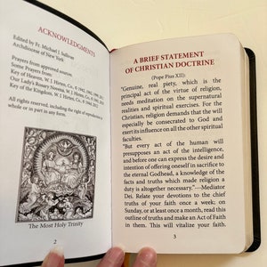 May include: Open book with black cover, displaying text and illustrations. The left page features an illustration of the Holy Trinity and the text "ACKNOWLEDGMENTS". The right page contains the text "A BRIEF STATEMENT OF CHRISTIAN DOCTRINE".