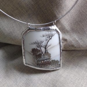 May include: A silver necklace with a rectangular pendant featuring a black and white illustration of a Japanese house with trees and a fence. The pendant is framed with a silver border.