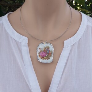 May include: A silver chain necklace with a white porcelain pendant featuring a vintage illustration of a couple in a romantic setting.