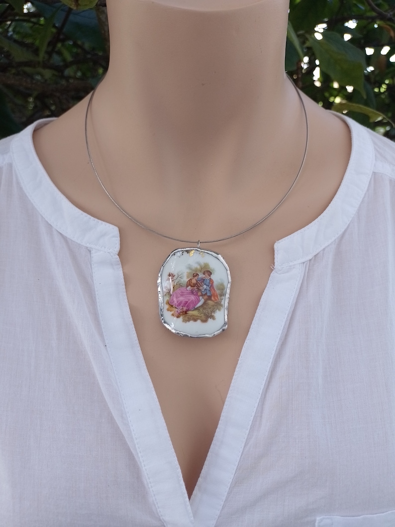 May include: A silver chain necklace with a white porcelain pendant featuring a vintage illustration of a couple in a romantic setting.