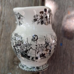 Pu&ograve; includere: Un'anfora in ceramica bianca con un motivo floreale bianco e nero e un'illustrazione in bianco e nero di una ragazza in un giardino.