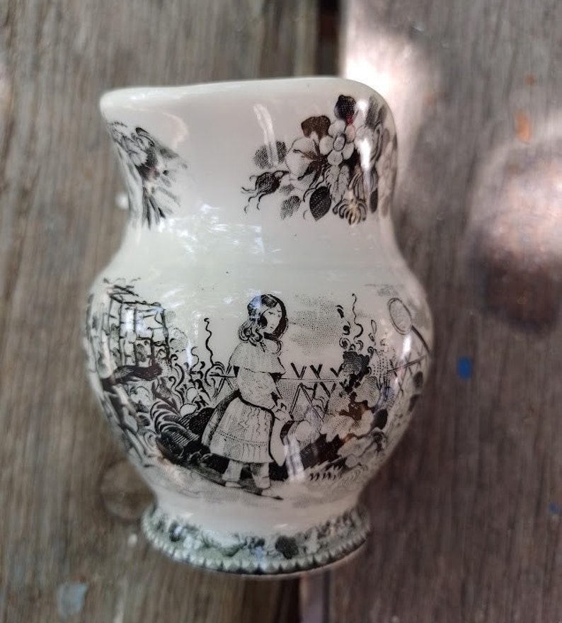 Pu&ograve; includere: Un'anfora in ceramica bianca con un motivo floreale bianco e nero e un'illustrazione in bianco e nero di una ragazza in un giardino.