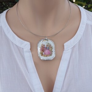 May include: A silver chain necklace with a porcelain pendant featuring a vintage illustration of a couple in a garden setting.