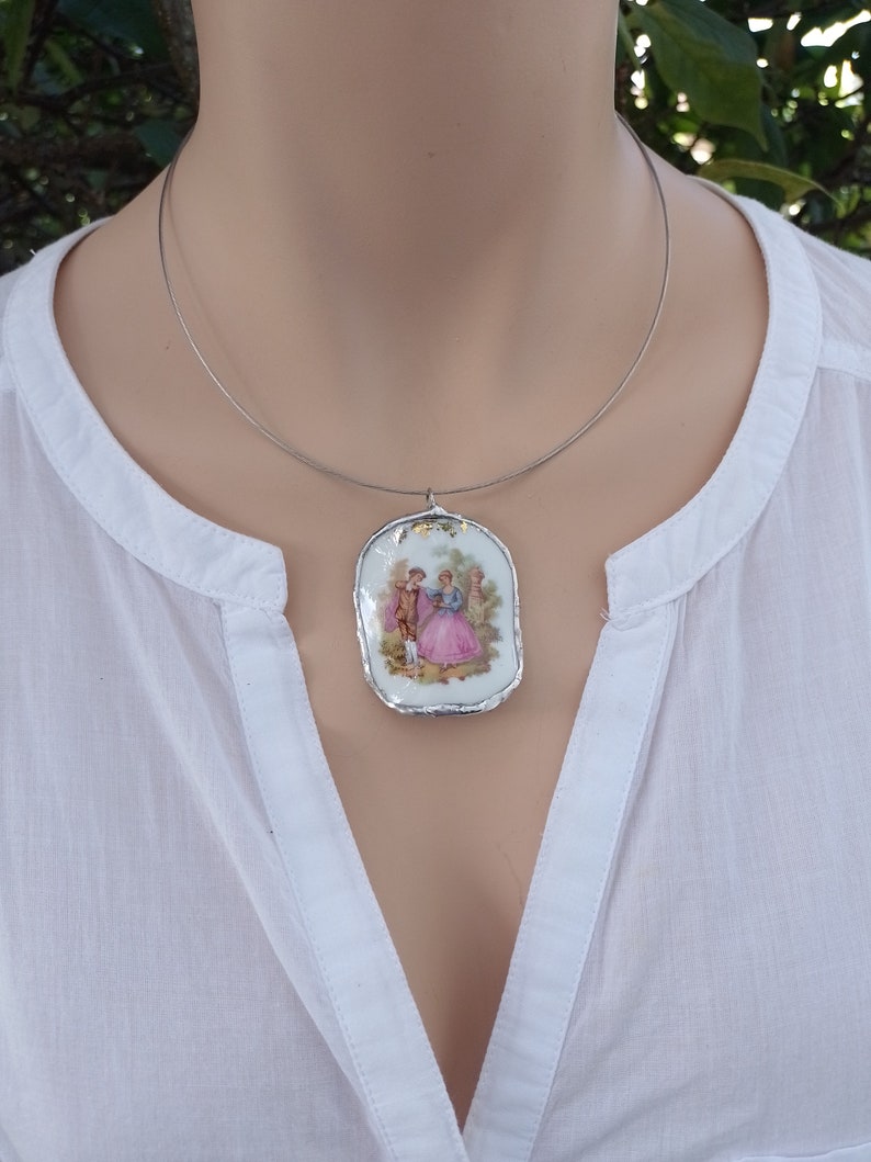 May include: A silver chain necklace with a porcelain pendant featuring a vintage illustration of a couple in a garden setting.