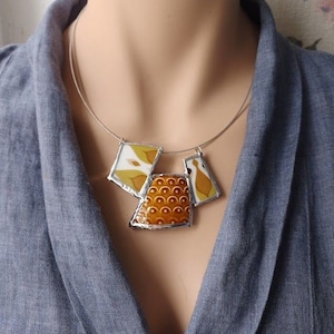 May include: A silver chain necklace with a geometric pendant made of white and brown ceramic tiles. The pendant is made up of three pieces, each with a different pattern.