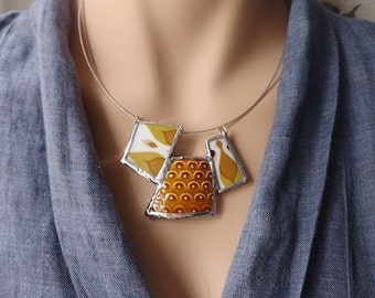 Può includere: Una collana con catena d'argento con un ciondolo geometrico in ceramica bianca e marrone. Il ciondolo è composto da tre pezzi, ognuno con un motivo diverso.