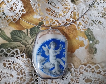 Può includere: Una collana d'argento con un ciondolo in porcellana blu e bianca raffigurante un cherubino alato che tiene un fiore. Il ciondolo ha la forma di una conchiglia.