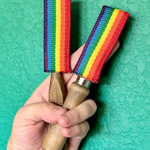 May include: Two wooden handled jump ropes with rainbow colored handles. The handles are made of woven fabric with red, orange, yellow, green, blue, indigo, and violet stripes.